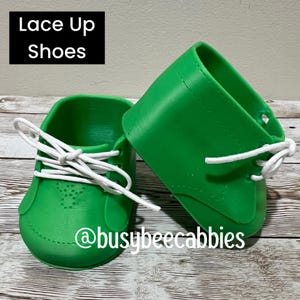 Może przedstawiać: Para jaskrawozielonych butów z białymi sznurowadłami, z tekstem "Lace Up Shoes" i "@busybeecabbies" nadrukowanym na obrazie. Buty mają gładką, formowaną konstrukcję z widocznymi detalami szwów i otworami na sznurowadła.