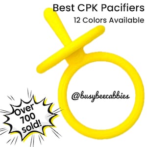 Puede incluir: Un chupete amarillo brillante con un mango circular y superficie texturizada. El texto dice: Best CPK Pacifiers, 12 Colors Available, @busybeecabbies y Over 700 sold! dentro de un gráfico de estrella. El diseño incluye un anillo.