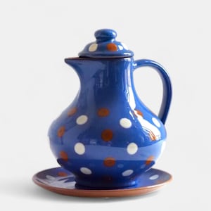 May include: A blue ceramic jug with a lid, handle, and matching saucer. The jug and lid are decorated with white and brown polka dots. The saucer is brown. The jug is likely used for serving beverages.