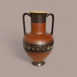 Puede incluir: Una ánfora de color terracota con dos asas. El jarrón presenta un cuello y una base de color marrón oscuro, con una banda de diseños circulares marrones oscuros y blancos alrededor del cuerpo. El borde es de color beige claro.