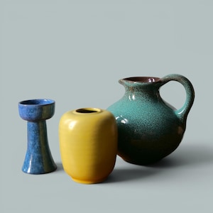 Peut inclure: Un ensemble de trois récipients en céramique : un grand bougeoir bleu moucheté, un vase jaune lisse et arrondi, et une grande carafe sarcelle mouchetée avec une anse incurvée. Chaque pièce présente une forme distincte et une finition émaillée.