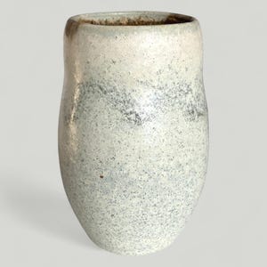 Könnte beinhalten: Eine handgefertigte Keramikvase mit einer gesprenkelten, strukturierten Oberfläche. Die Vase hat ein hellgraues und weißes Farbschema mit einem dunkleren grauen Band in der Mitte. Die Öffnung ist dunkelbraun.