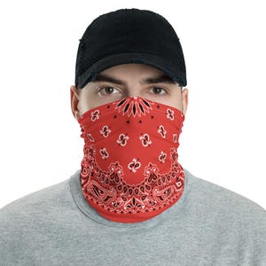May include: A red bandana face covering with a black and white paisley pattern. The face covering is worn by a person wearing a black baseball cap and a grey shirt. The bandana covers the nose and mouth.