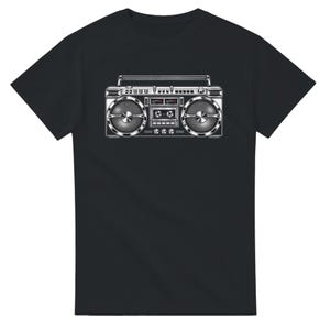 May include: A black short-sleeved t-shirt featuring a central graphic print of a vintage-style boombox. The boombox illustration is rendered in shades of silver, grey, and black, showcasing two large circular speakers, a cassette deck, and control dials.