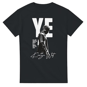 May include: A black short-sleeved t-shirt featuring a large white 'YE' graphic, a silhouette of a person, and the text 'TELLING TRUTH IS CRAZY IN A WORLD FULL OF LIES' alongside the signature 'Kanye West' printed in white on the front centre.