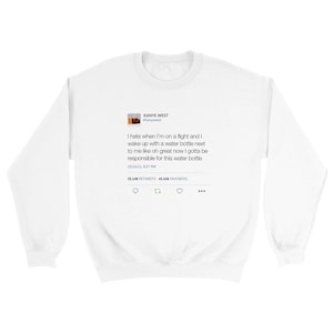 May include: White sweatshirt featuring a printed tweet by Kanye West. The tweet reads, "I hate when I'm on a flight and I wake up with a water bottle next to me like oh great now I gotta be responsible for this water bottle."