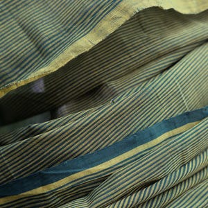 Peut inclure: Gros plan sur un tissu plié avec un motif à rayures dans les tons de bleu sarcelle et or. Le tissu a un aspect doux et texturé, avec des rayures horizontales. Les plis créent des ombres et de la profondeur.