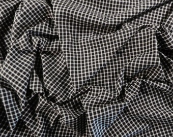 May include: Close-up of a black and white checked fabric. The fabric is draped and wrinkled, creating shadows and texture. The pattern is a classic gingham design, with small, evenly spaced squares.