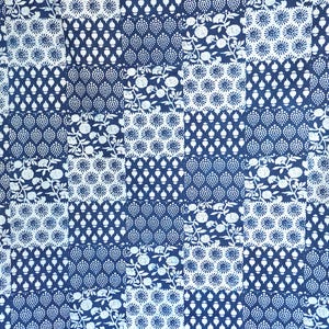 Op de afbeelding: Een marineblauwe stof met een patchwork-ontwerp. Het patroon bevat witte bloemen en geometrische vormen gerangschikt in een raster. Het herhalende ontwerp creëert een symmetrische lay-out. De stof is waarschijnlijk katoen of een vergelijkbaar materiaal.