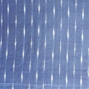 May include: Blue fabric featuring a white ikat pattern. The fabric has vertical stripes of white diamond shapes against a blue background. The fabric is likely cotton or linen.