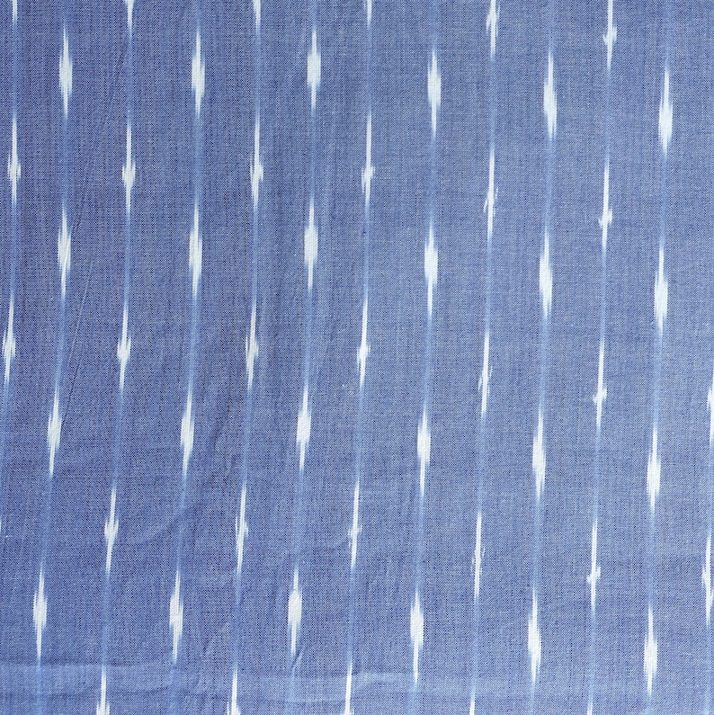 May include: Blue fabric featuring a white ikat pattern. The fabric has vertical stripes of white diamond shapes against a blue background. The fabric is likely cotton or linen.