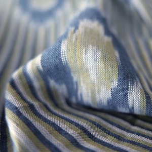 May include: Close-up of a folded fabric with a blue, white, and olive green striped pattern. The fabric has a textured appearance and a subtle ikat design. The stripes run vertically, creating a sense of depth and movement.