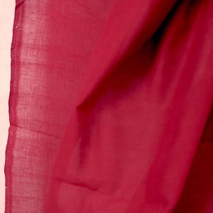 Könnte beinhalten: Nahaufnahme eines fließenden, tiefroten Stoffes. Das Material scheint leicht zu sein, mit sichtbarer Textur und leichtem Glanz. Die Falten und Drapierungen erzeugen Schatten, die die Tiefe und das visuelle Interesse des Textils verstärken.