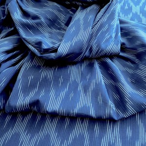 May include: A close-up shot of a folded, navy blue fabric with a white, vertical stripe design. The material has a subtle sheen, and the folds create shadows and depth. The texture appears soft and flowing, suggesting a textile suitable for clothing or home decor.