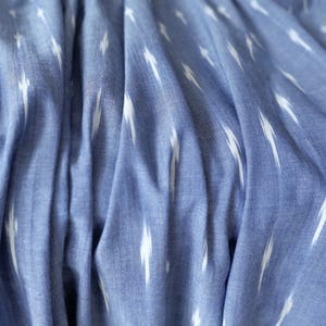 May include: Close-up of blue fabric with white, lightning bolt-shaped patterns. The fabric is textured and appears to be slightly wrinkled, with soft folds and shadows. The overall colour palette is a light blue with white accents.