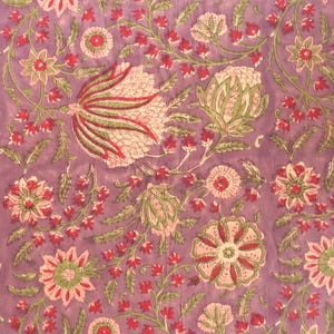 May include: Close-up of a floral fabric with a lavender background. The design features pink, red, and green flowers and leaves. The pattern is detailed and intricate, with a vintage or bohemian aesthetic.