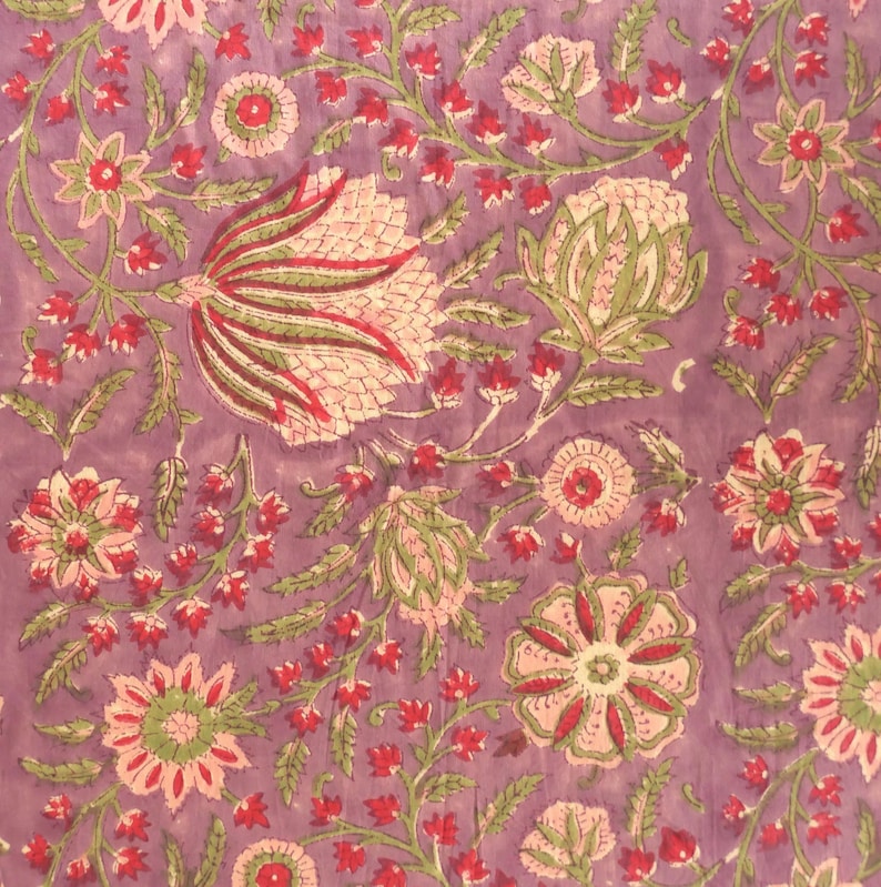 May include: Close-up of a floral fabric with a lavender background. The design features pink, red, and green flowers and leaves. The pattern is detailed and intricate, with a vintage or bohemian aesthetic.