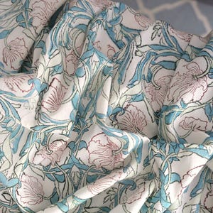 Può includere: Tessuto bianco con un motivo floreale ripetuto in rosa, azzurro e verde. Il design presenta fiori e foglie stilizzate, creando un'estetica morbida e fluida. Il tessuto è probabilmente cotone o lino.