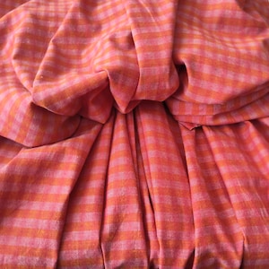 Könnte beinhalten: Nahaufnahme eines gefalteten Stoffes mit einem Streifenmuster in Rosa- und Orangetönen. Der Stoff ist zerknittert, wodurch ein strukturierter und geschichteter Effekt entsteht. Die Streifen verlaufen horizontal.