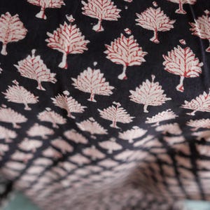 Könnte beinhalten: Nahaufnahme eines Stoffes mit einem sich wiederholenden Baummuster. Die Bäume sind weiß mit roten Details, vor einem schwarzen Hintergrund. Der Stoff wirkt weich, möglicherweise Baumwolle, mit einer leichten Textur.