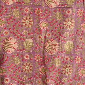 May include: Close-up of a floral fabric with a lavender background. The pattern features stylized flowers and foliage in shades of red, green, and pink. The design is repeated across the fabric, creating a visually rich and textured surface.