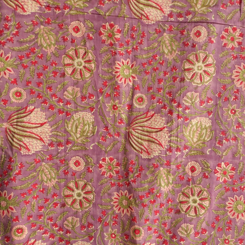 May include: Close-up of a floral fabric with a lavender background. The pattern features stylized flowers and foliage in shades of red, green, and pink. The design is repeated across the fabric, creating a visually rich and textured surface.
