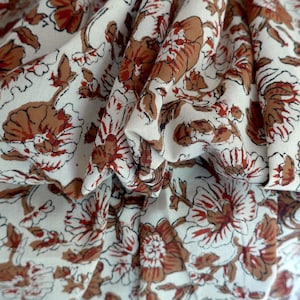 May include: Close-up of a white fabric with a repeating floral pattern in shades of brown and red. The fabric is gathered, creating folds and shadows that highlight the design. The floral pattern is detailed and intricate.