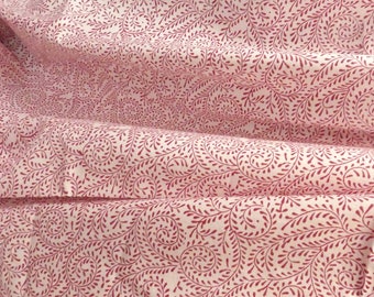 May include: Close-up of a fabric with a repeating pattern of burgundy-colored, stylized leaves and vines on a cream background. The fabric is folded, showing the texture and depth of the material. The design is reminiscent of a botanical print.