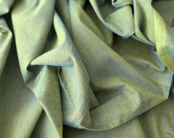 May include: Close-up of a textured fabric in shades of green and blue. The fabric is arranged in folds, creating shadows and highlighting its texture and colour variations. The overall appearance suggests a soft, flowing material.
