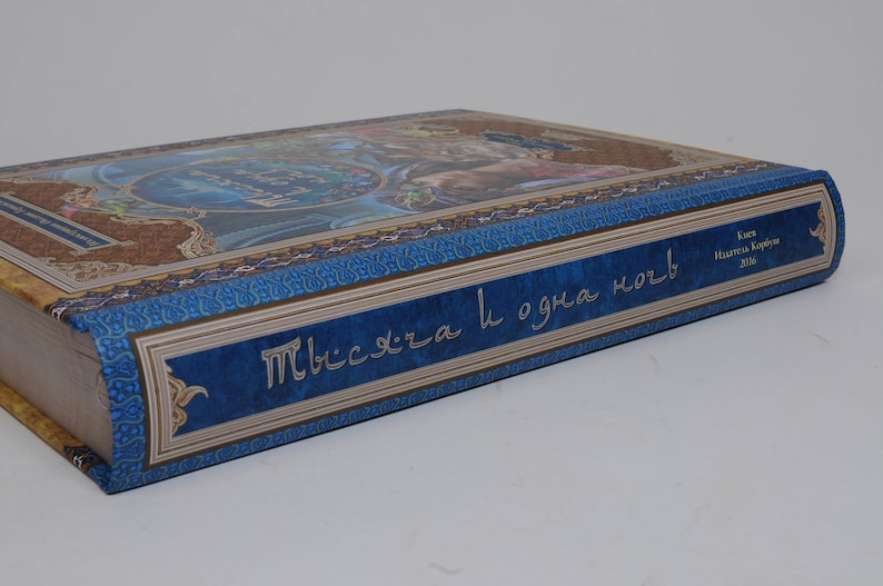 May include: A hardcover book with a blue and gold cover featuring ornate designs and text in a foreign language. The spine has text in a contrasting color. The book's edges are visible.