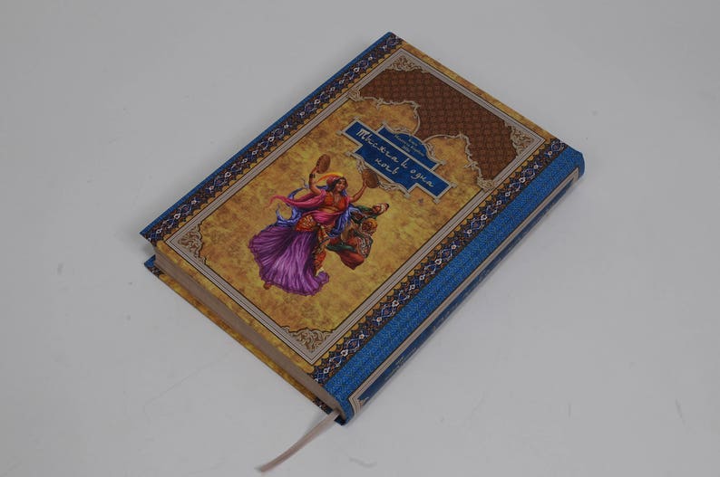 May include: Hardcover book with a blue spine and cover accents. The cover features a colorful illustration of a woman riding a creature, with text in a blue banner. A cream-colored ribbon bookmark is visible.