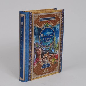 May include: Hardcover book with a blue spine and cover featuring an illustration of a woman, a tiger, and a palace. The cover has gold and brown decorative elements and text in a foreign language.