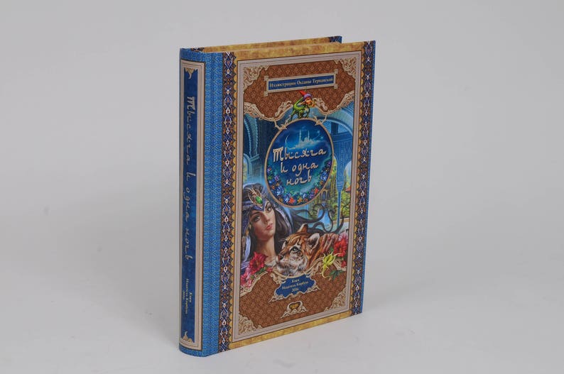 May include: Hardcover book with a blue spine and cover featuring an illustration of a woman, a tiger, and a palace. The cover has gold and brown decorative elements and text in a foreign language.
