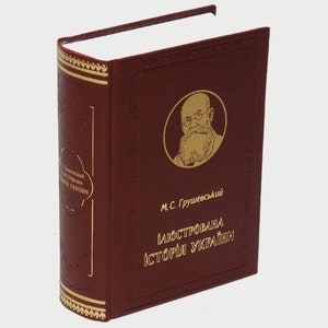 Puede incluir: Un libro encuadernado en cuero rojo con detalles dorados y un retrato de un hombre con barba y gafas. El título del libro es "Ілюстрована історія України" de М.С. Грушевський.