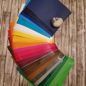 May include: A fan of colourful vinyl sheets in various shades of blue, green, yellow, orange, red, brown, and purple. The sheets are arranged in a fan shape with the darkest blue sheet on top and the lightest green sheet on the bottom.