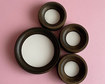 May include: Four dark brown wooden picture frames with white mats and rounded edges. The frames are arranged in a cluster on a pink background.