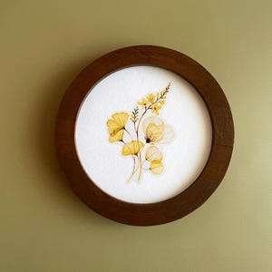 May include: A framed watercolor painting of yellow flowers with a white background. The frame is made of dark wood.