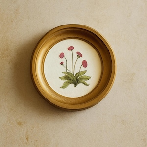 May include: A circular gold-toned frame containing a circular off-white insert. The insert features a botanical illustration of a plant with green leaves and five small, round, dark pink flower heads on thin, upright stems centered in the frame.