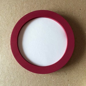 May include: A round, red wooden frame with a white center. The frame is perfect for displaying photos or artwork.
