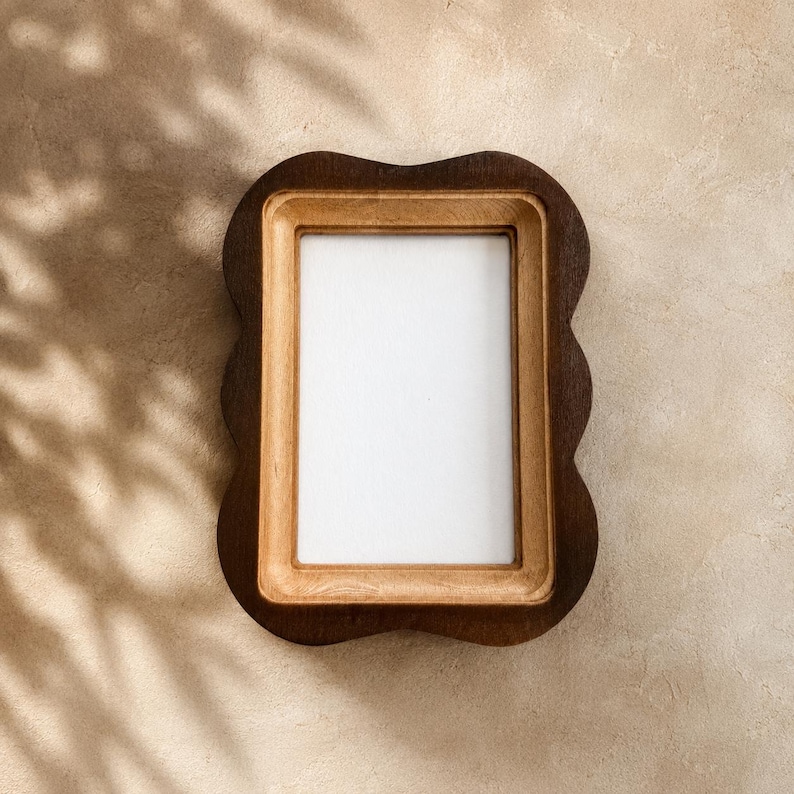 May include: A rectangular wooden picture frame featuring a dark brown outer border with a scalloped edge and a lighter natural wood inner border surrounding a blank white rectangular center space for displaying photographs or artwork.