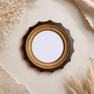 May include: A circular wooden frame featuring a dark brown outer edge with a scalloped, sunburst-like design and a lighter, natural-toned inner ring surrounding a blank, white circular centre space for displaying a photograph or artwork.