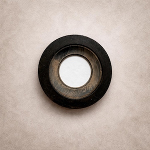 May include: A circular wooden object with a dark, stained outer ring and a lighter, natural wood inner ring. The centre features a white circle. The object is set against a neutral, textured background.