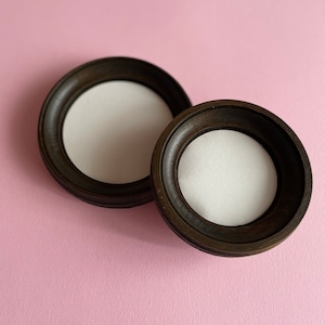 May include: Two dark brown wooden picture frames with white mounts. The frames are round and have a simple design.