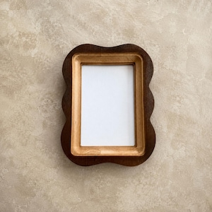 May include: A rectangular picture frame with a wavy, scalloped outer edge. The frame features a dark brown outer border and a lighter, natural wood-toned inner border surrounding a plain white rectangular center insert for a photograph.