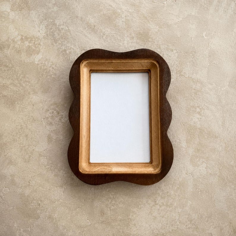 May include: A rectangular picture frame with a wavy, scalloped outer edge. The frame features a dark brown outer border and a lighter, natural wood-toned inner border surrounding a plain white rectangular center insert for a photograph.