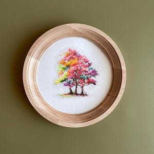 May include: A framed watercolor painting of three trees with colorful leaves in shades of pink, red, yellow, and green. The trees are set against a white background.