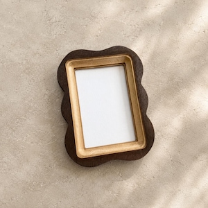 May include: A rectangular picture frame with a dark brown, wavy outer edge and a light tan, smooth inner border. The frame features a central white rectangular insert, providing a clear space for a photograph or artwork within the wooden structure.