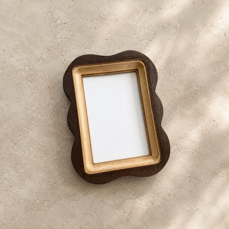 May include: A rectangular picture frame with a dark brown, wavy outer edge and a light tan, smooth inner border. The frame features a central white rectangular insert, providing a clear space for a photograph or artwork within the wooden structure.