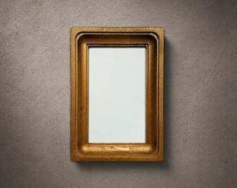 May include: A rectangular picture frame with a metallic gold finish and a deep, stepped inner border. The frame features a smooth, solid construction with a clean, centred rectangular opening that displays a plain white background surface.
