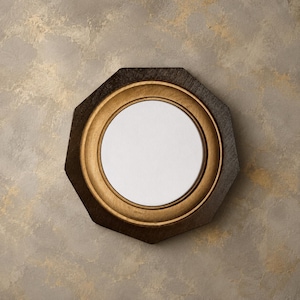 Puede incluir: Un espejo de pared octogonal con un marco de madera oscura y texturizada que rodea un borde interior circular de tono dorado. La superficie reflectante central es clara y circular, destacando sobre la forma geométrica del marco exterior.